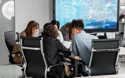 Profissionais reunidos em mesa com laptop mostrando diagrama de fluxo de chatbot e ícone do WhatsApp
